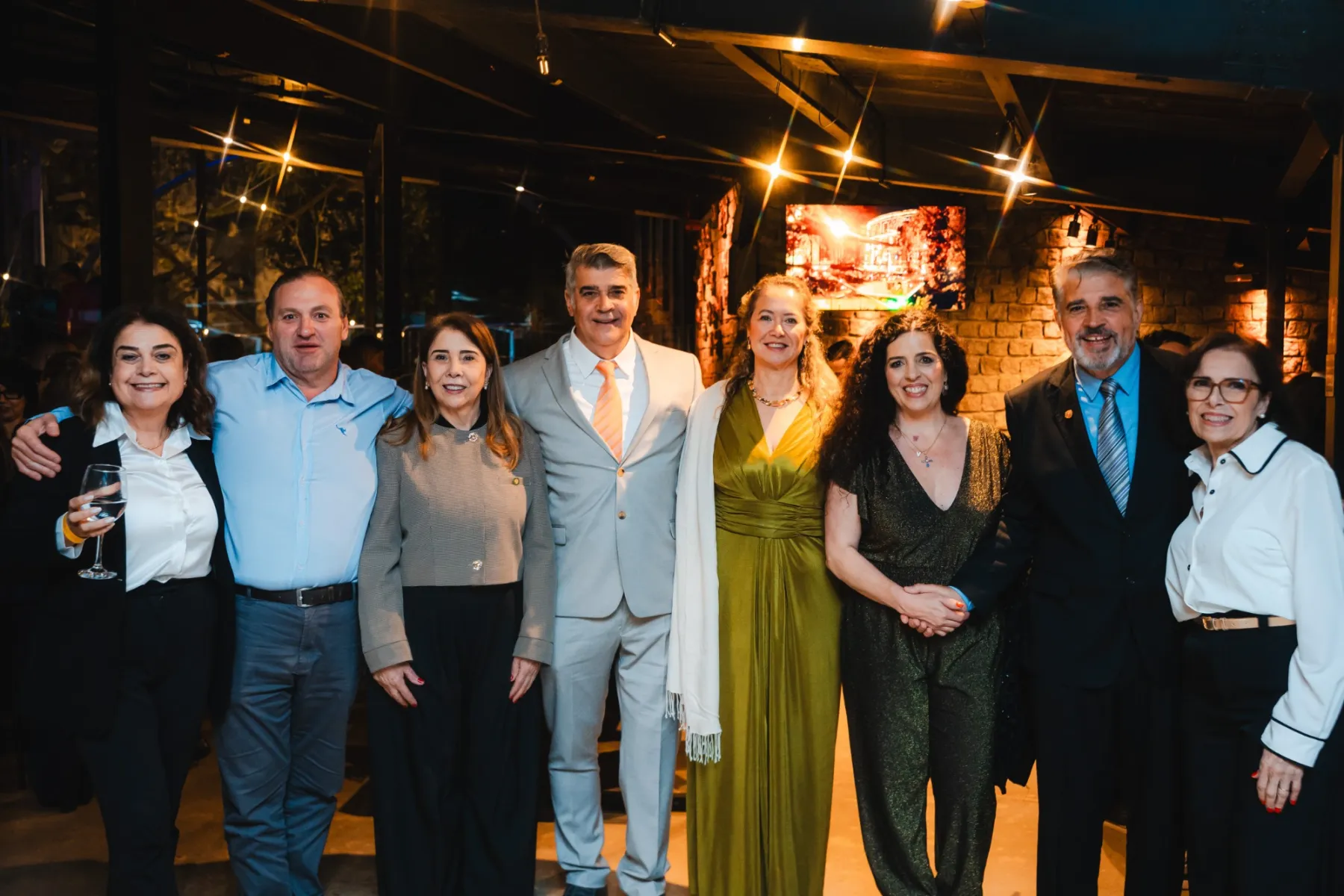 Oito pessoas da família Canabrava lado a lado, sorrindo, no salão iluminado por luzes amarelas