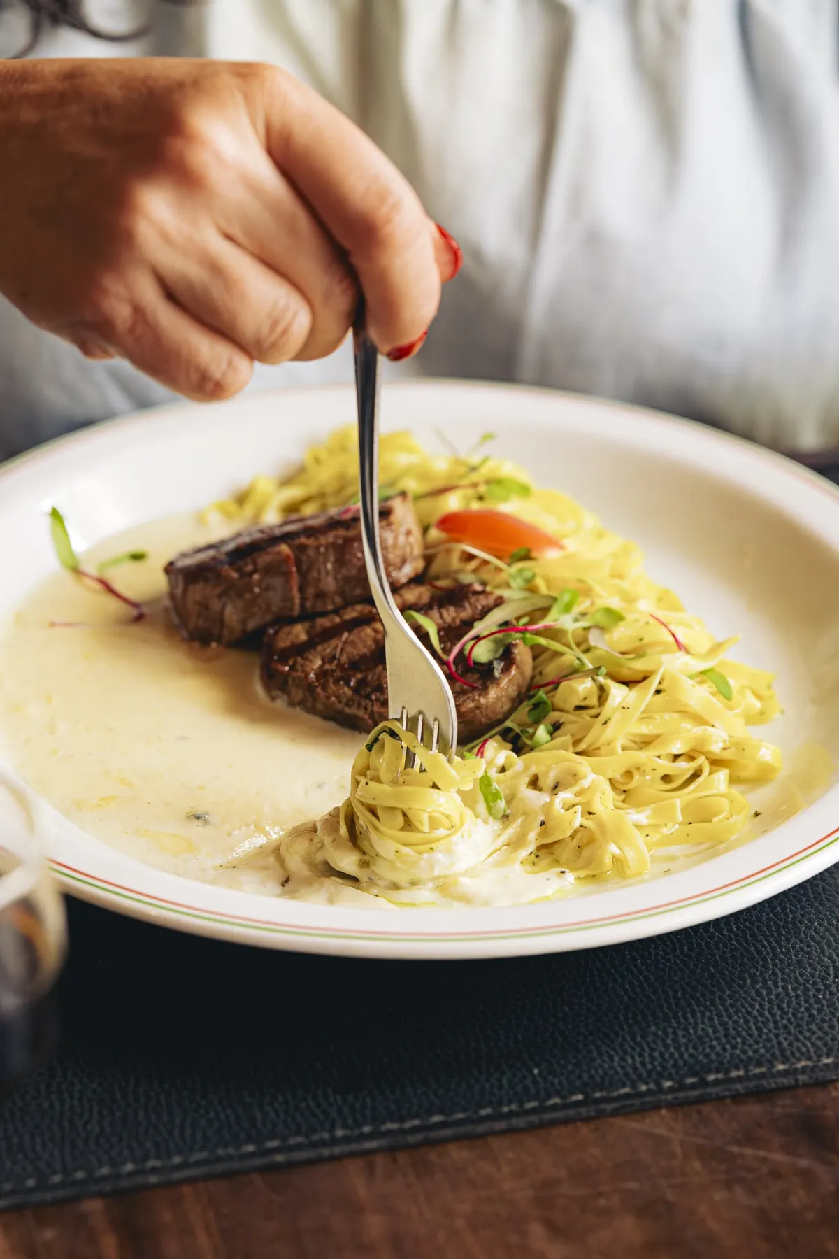 Garfo enrolando fettuccine ao lado de um filé, em luz dourada